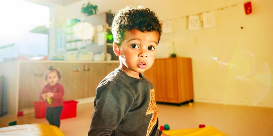 Een kind kijkt in de lens en speelt samen met een ander kind.